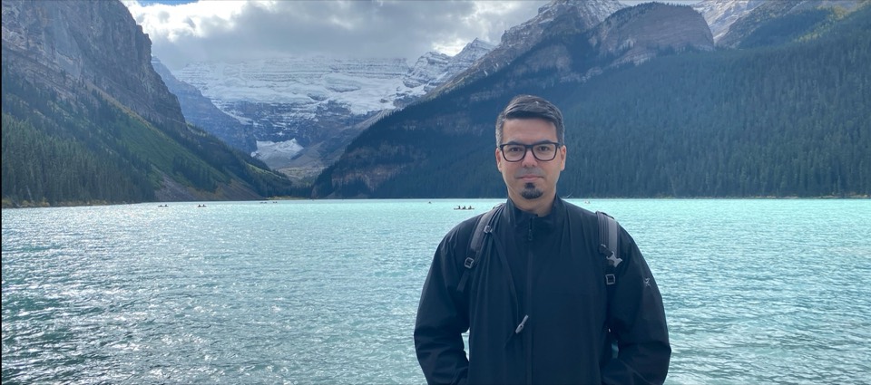 Victor standing by a turquoise lake in the mountains of Banff National Park